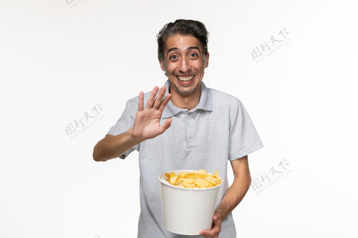 年轻男性正面图：年轻的男性正在吃薯片 在白色的表面上欢笑男性杯子员工