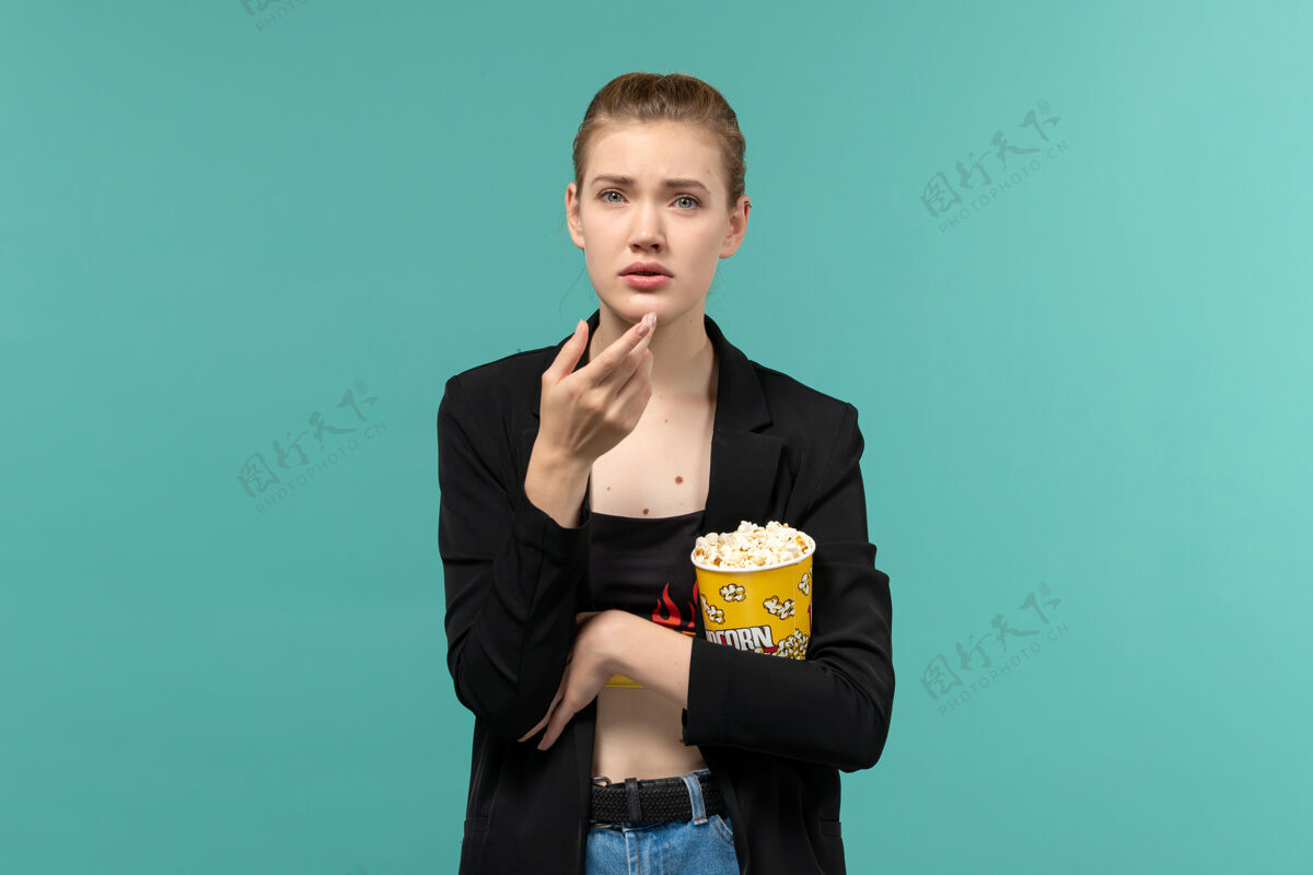 包装前视图年轻女性手持爆米花包在浅蓝色表面看电影前抱电影