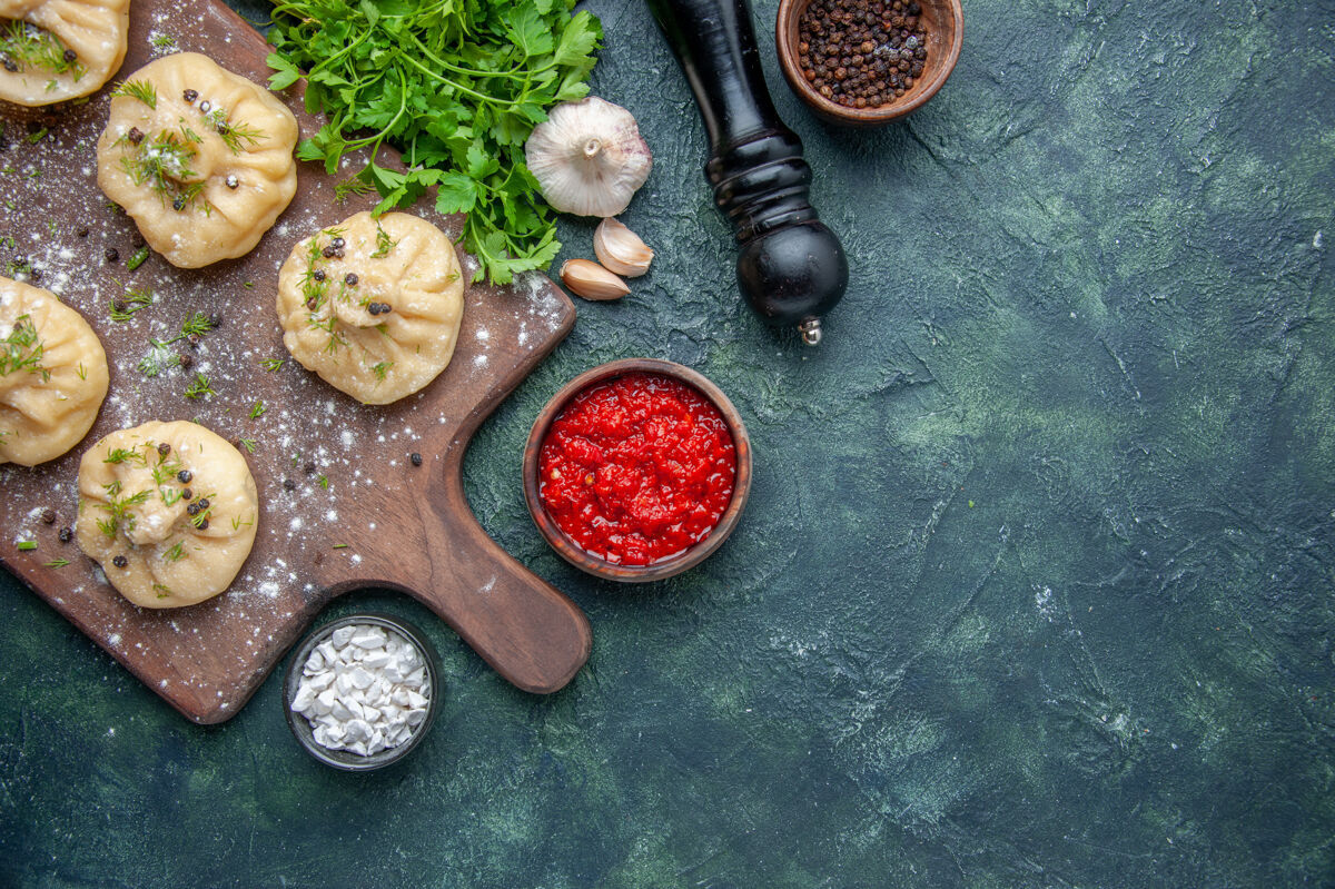 一餐俯瞰图：深蓝色背景上有番茄酱和绿色的生水饺烹饪晚餐面团菜肉食盘子肉背景