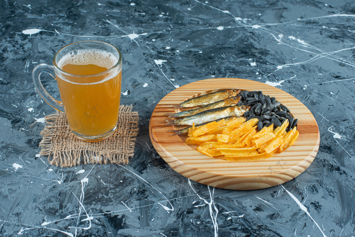 美味一杯啤酒放在质地上 开胃菜放在木制盘子上 蓝色背景烤新鲜美味