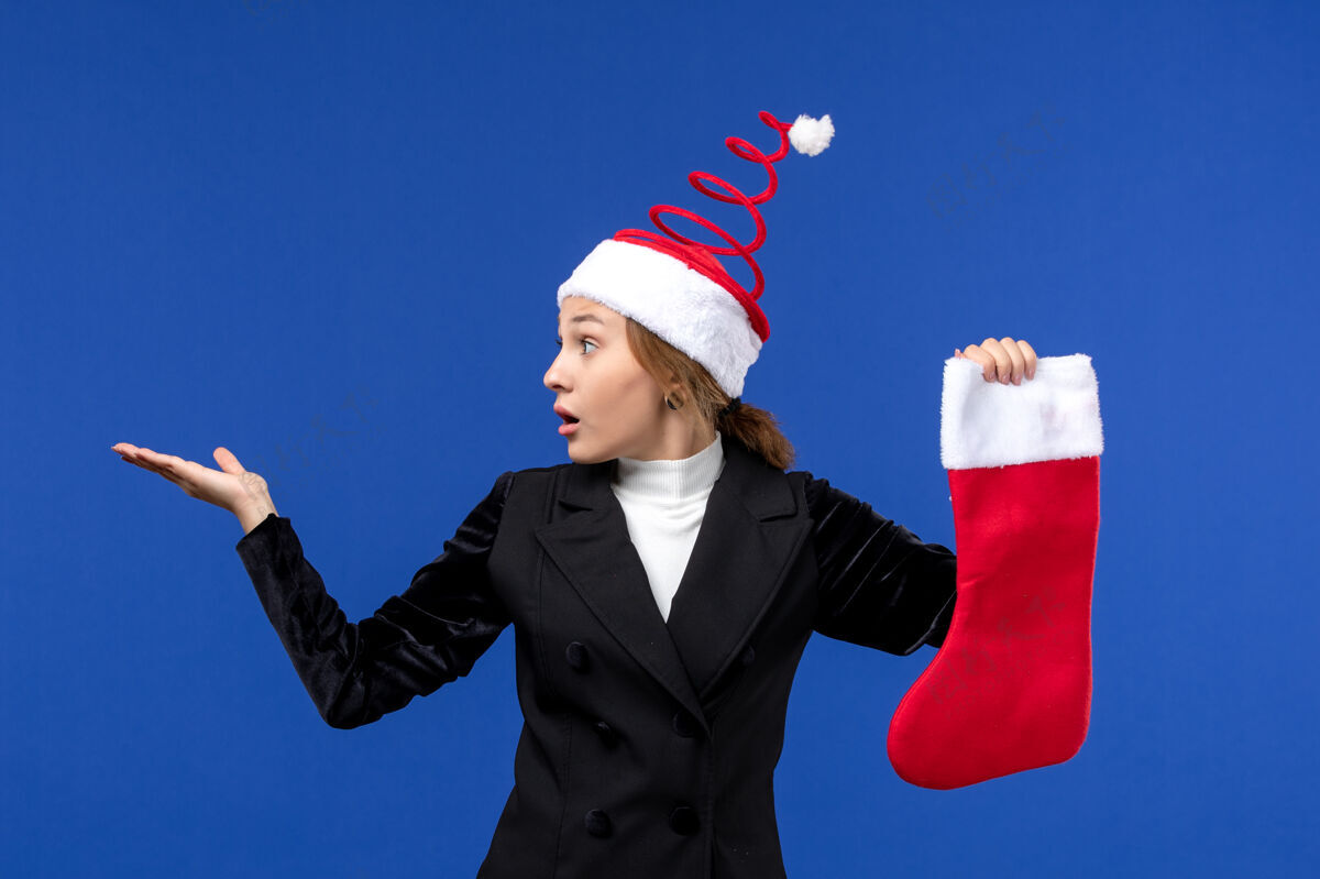 爱国正面图：年轻女子手持红色圣诞袜站在蓝色墙壁上过年西装商人成功