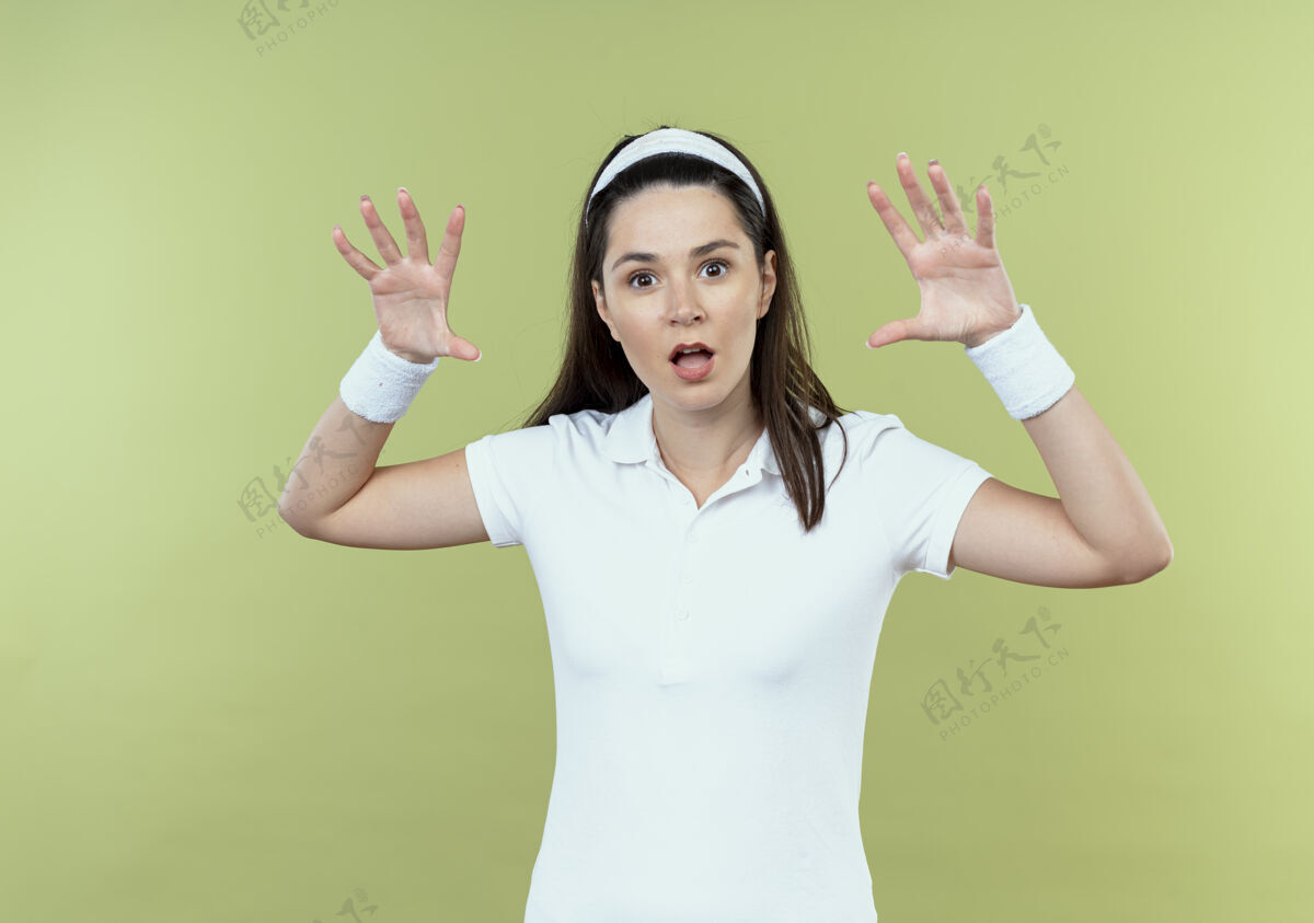 年轻戴着头巾的年轻健身女士举手威胁站在轻质墙上手女子头带