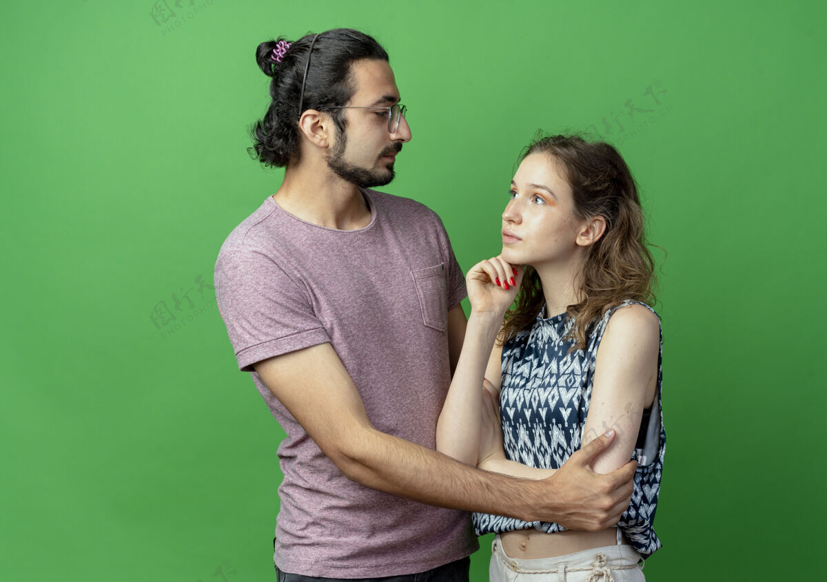 男人一对年轻的男女幸福的男人拥抱着他的女朋友 而她站在绿色的墙上沉思的表情情侣女人年轻