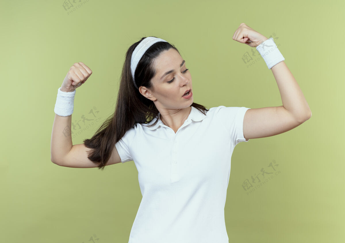 拳头戴着头巾的年轻健身女士举起拳头 站在轻薄的墙壁上 露出自信的二头肌二头肌女人展示
