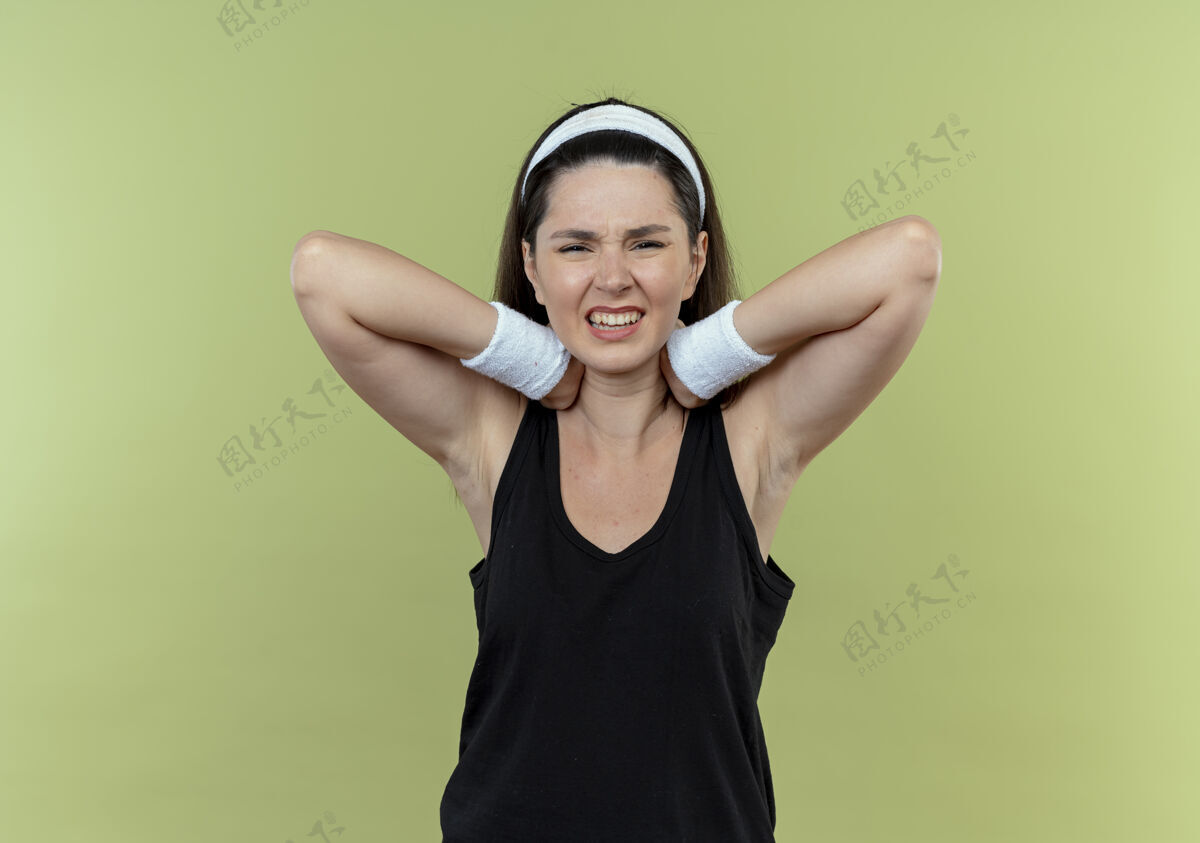 颈部戴着头巾的年轻健身女士站在轻质墙壁上摸着她的脖子 看起来不舒服 感觉疼痛头带健身感觉