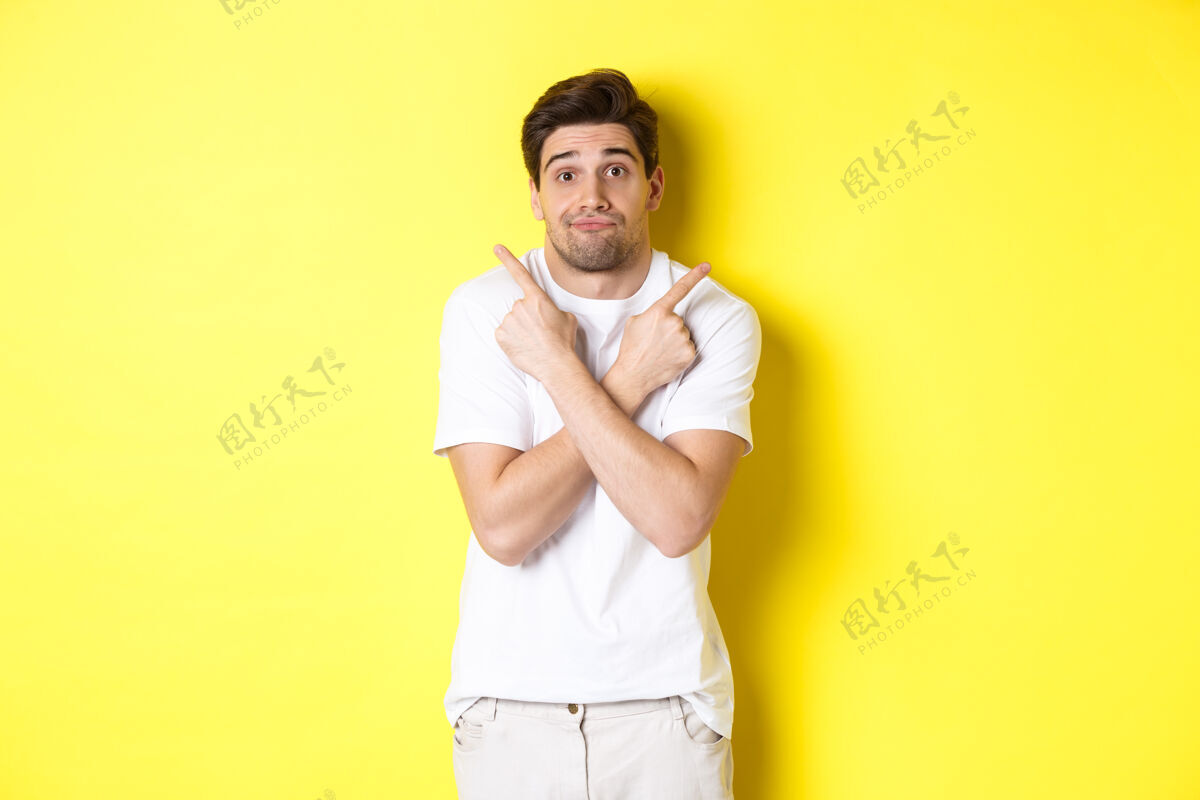 时尚优柔寡断的男人横着手指 挣扎着做决定 征求意见 站在黄色的背景上表情成人指