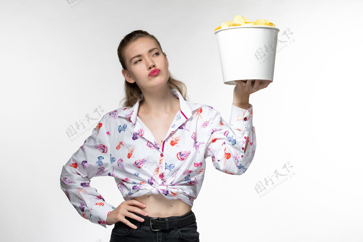 篮子正面图：白色表面上拿着薯片的年轻女性手提篮享受前面土豆