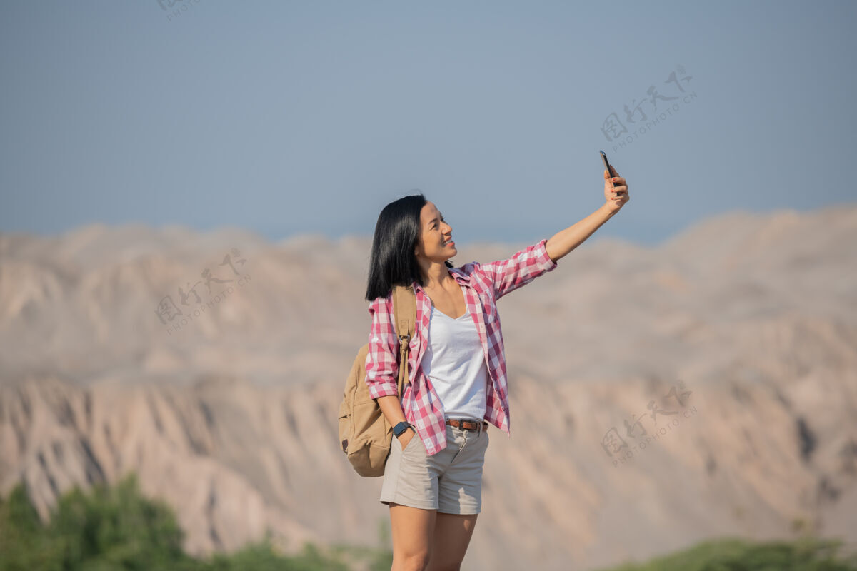 徒步旅行者徒步登山的女人背着背包 拿着杆子站在石峰岭上眺望风景 快乐的女人在山上自拍自然冒险乡村