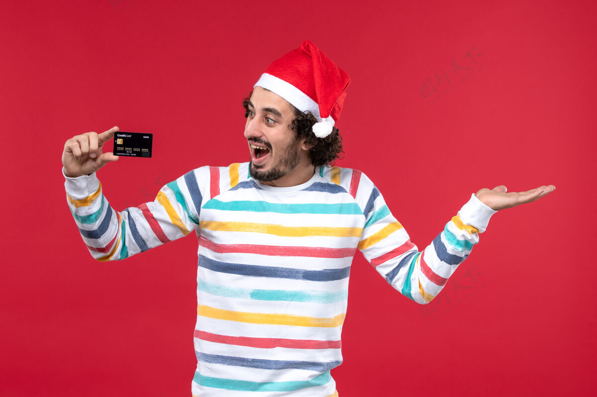 看法正面图年轻男子手持银行卡在红墙上感慨红男节日男性银行圣诞节