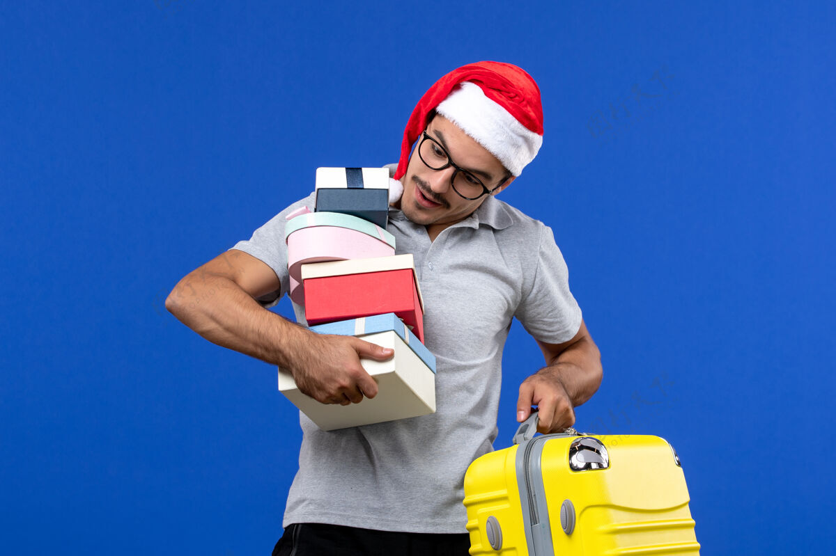 包前视图年轻男性手持礼物和包在蓝色背景飞机上飞行度假工作建筑商工头