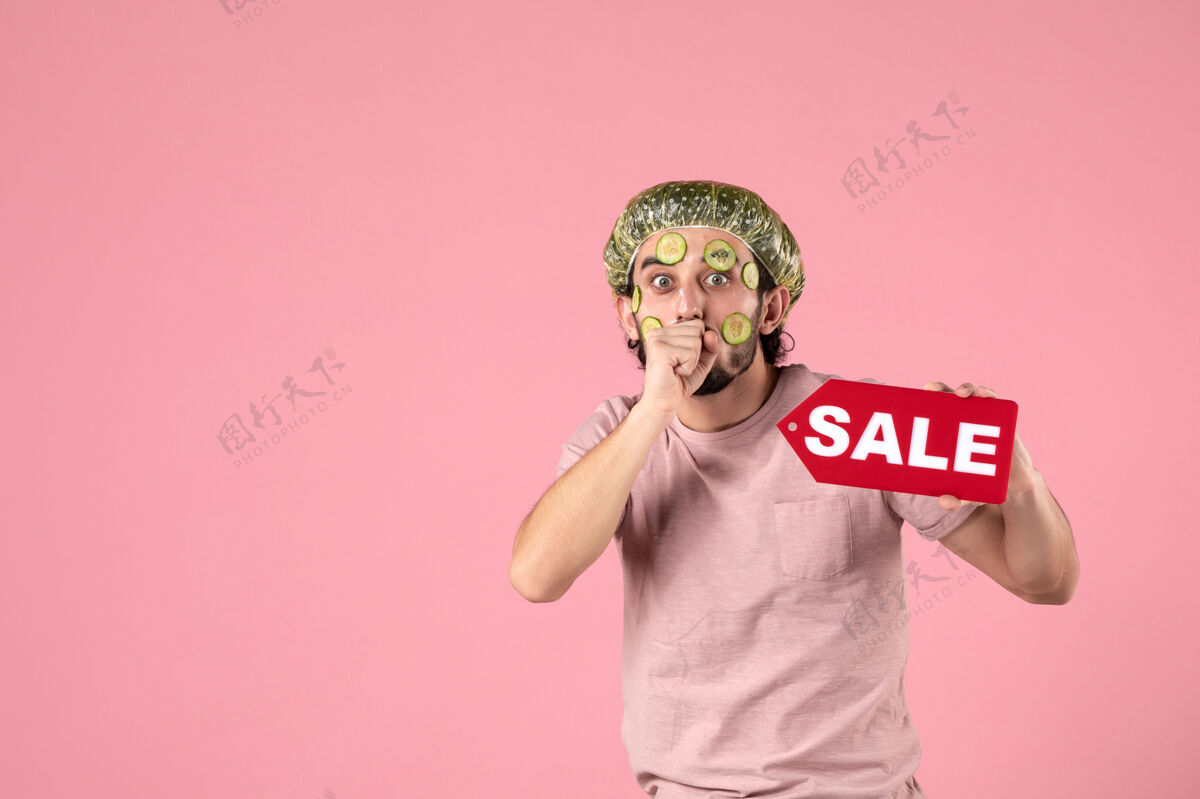 黄瓜正面图：年轻男性 脸上戴着面具 手持粉色背景的销售铭牌面部身体脸