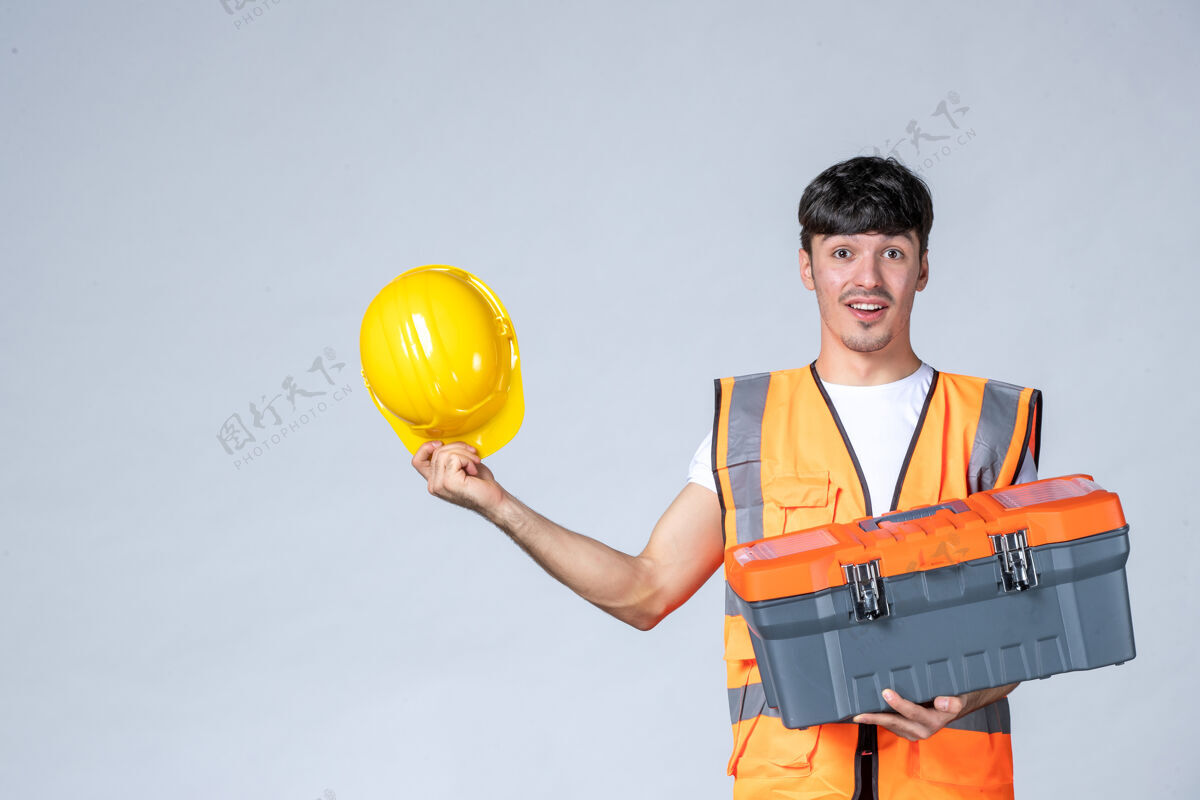 机械师正面图：年轻的男工人拿着沉重的工具箱 背景是白色的人工作箱子
