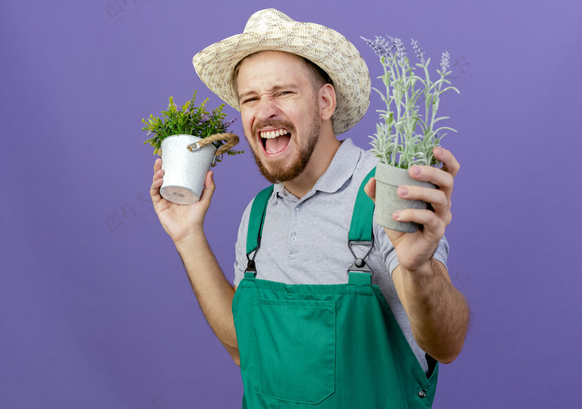 制服年轻英俊的斯拉夫园丁穿着制服 戴着帽子 拿着花盆 尖叫着孤立地站在紫色的墙上 留着复制空间花园拿着尖叫