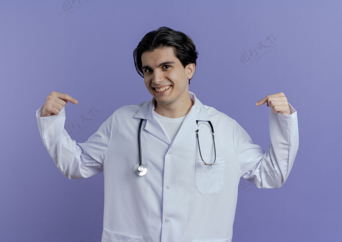 指着面带微笑的年轻男医生穿着医用长袍 戴着听诊器 指着隔离在紫色墙上的自己医生医疗男性