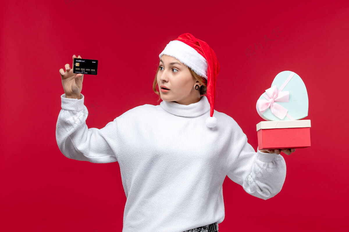礼物正面图红色背景上的年轻女性 带着银行卡和礼物微笑欢呼肖像