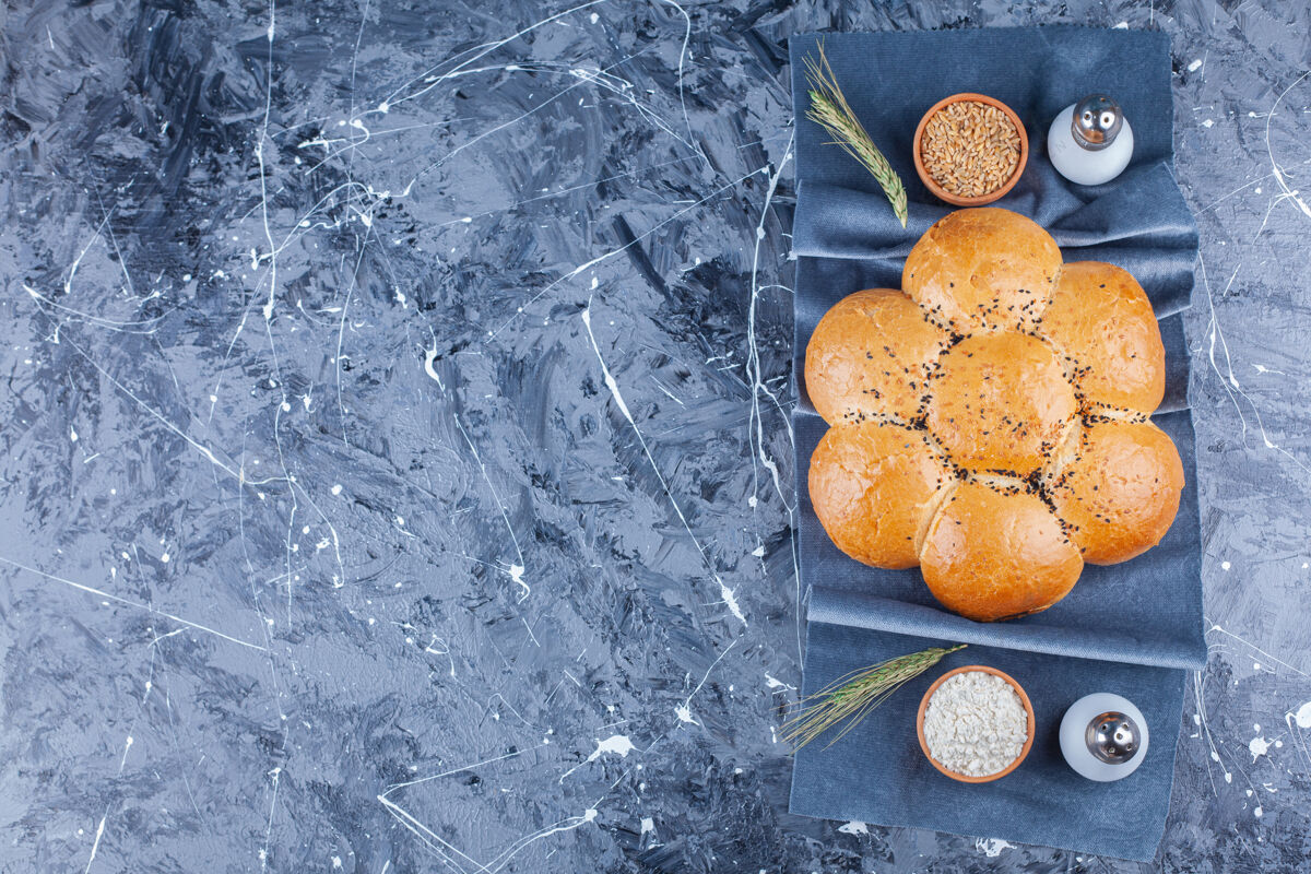 面团圆形花形面包 盐 面粉和谷物上的布片上的蓝色面包可口顶视图