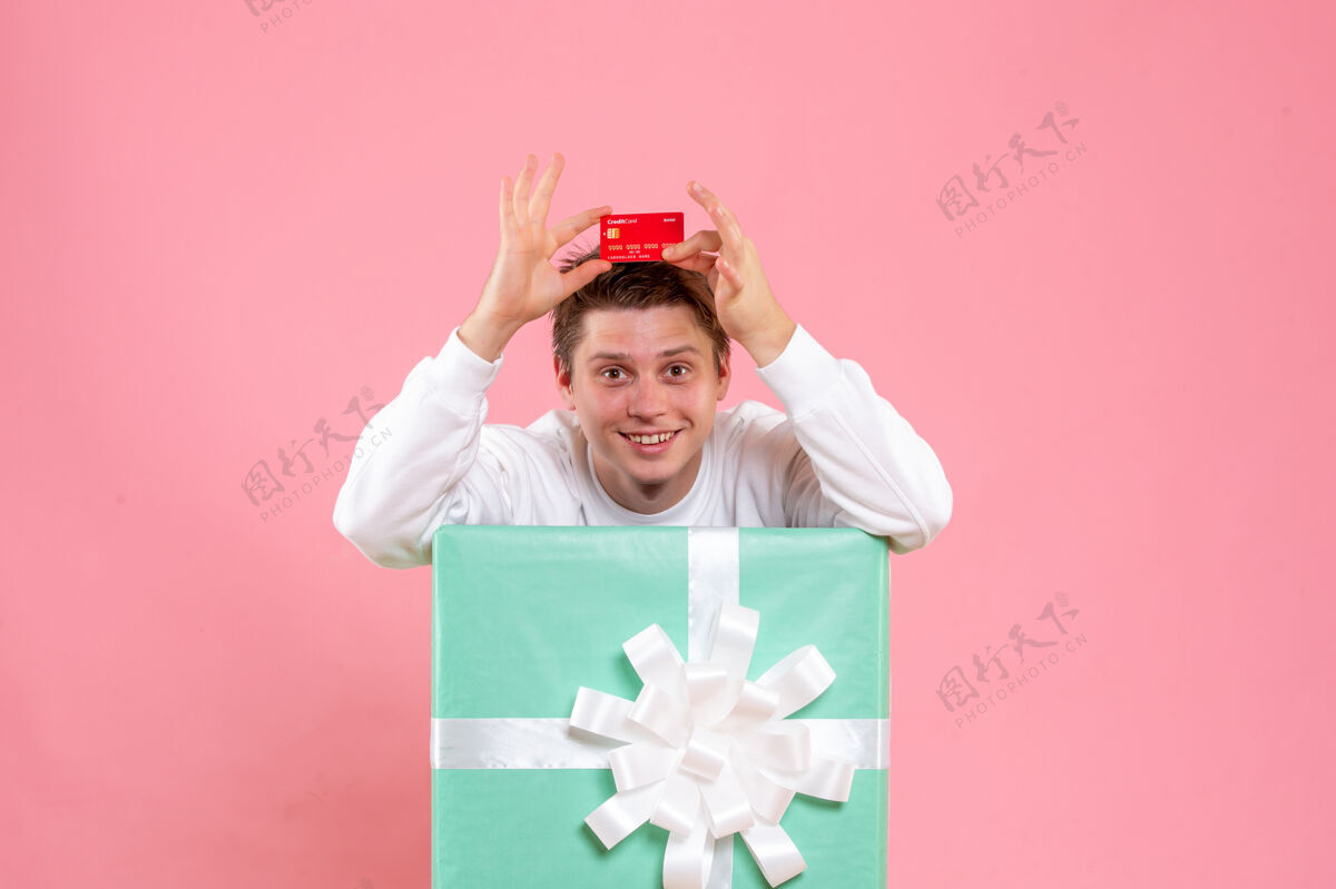银行正面图里面的年轻男性在粉红色的桌子上拿着红色的银行卡红色圣诞持有