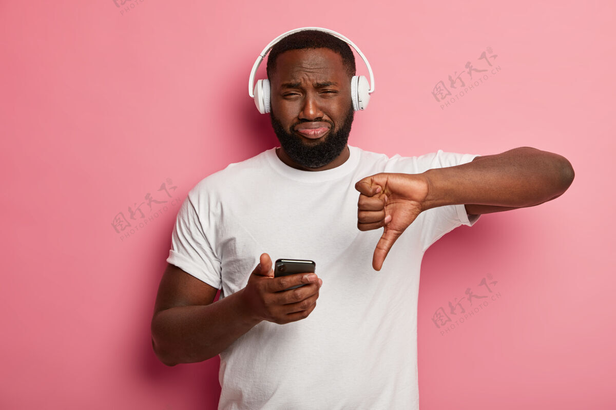 站立不满的胡子黑人表现出厌恶的姿态 不喜欢播放列表中的歌曲 听到耳机里的声音耳机男人播放器