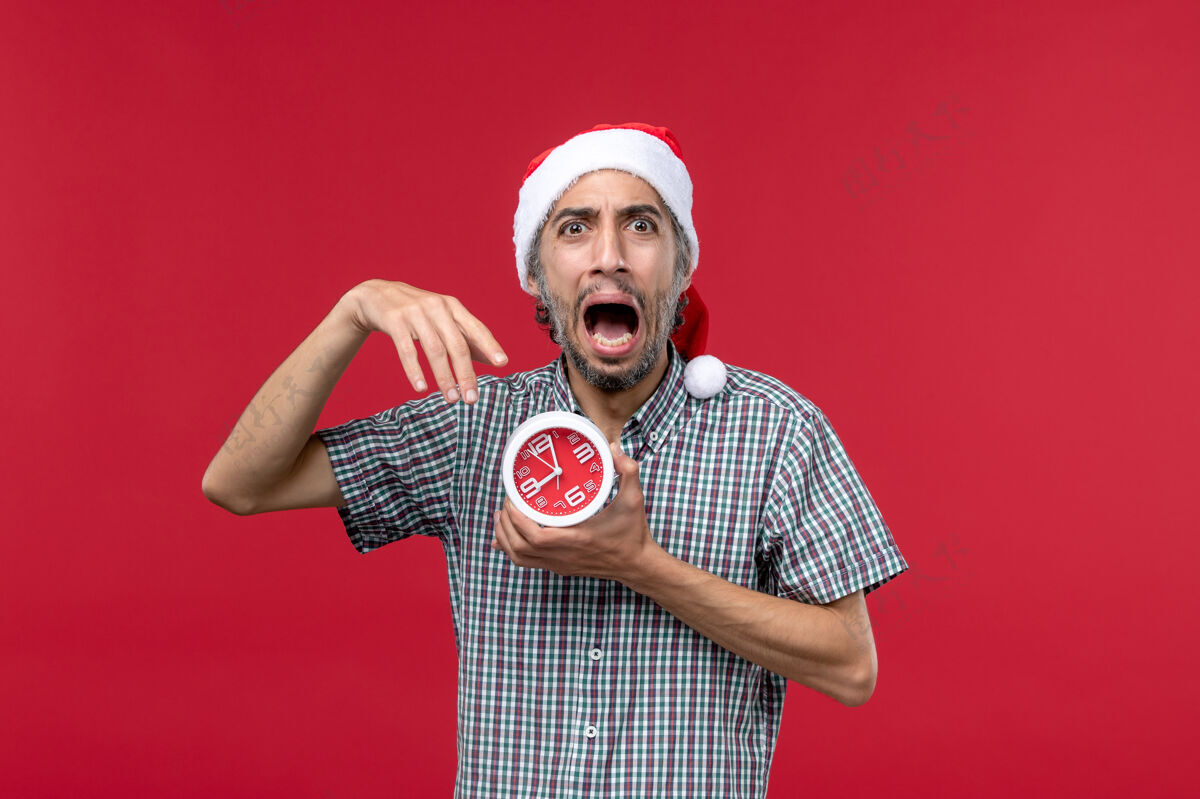 情绪正面图红色背景上的年轻男性 带着圆形的时钟男人圣诞男性