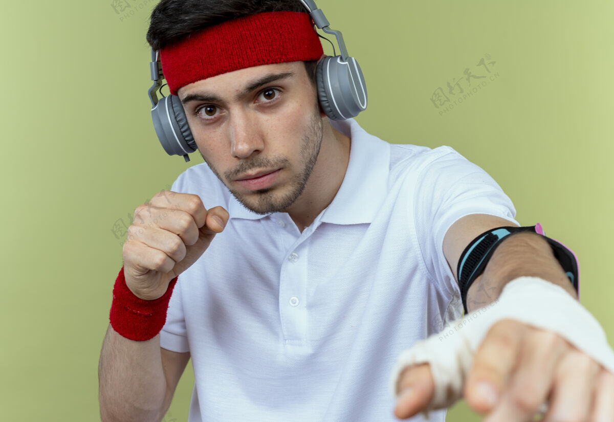 拳头戴着头戴式耳机和智能手机臂带的年轻运动型男子 摆出一副拳手紧握果岭的架势年轻战士移动