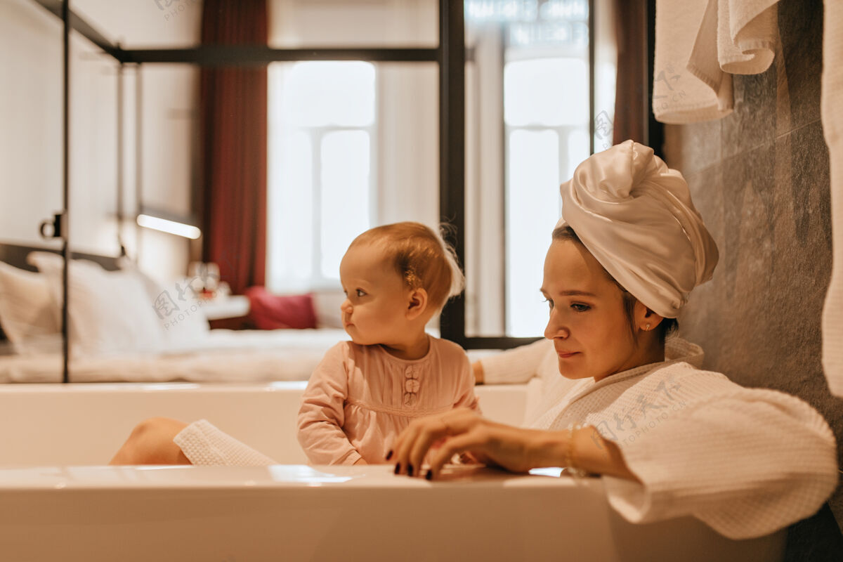 浴缸妈妈和女儿坐在雪白的浴缸里头上裹着毛巾的女人抱着孩子年轻人女儿房间