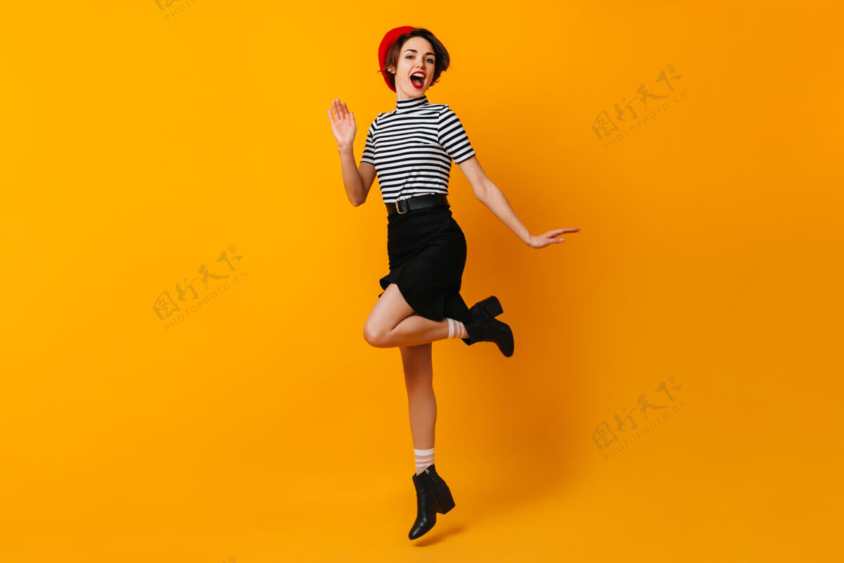 笑悠闲的法国女人穿着裙子在黄色的墙上跳舞乐趣休闲手势