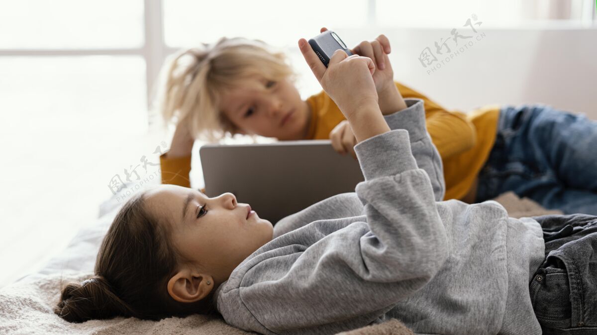 室内兄弟姐妹在床上玩手机和平板电脑小玩意平板电脑女孩