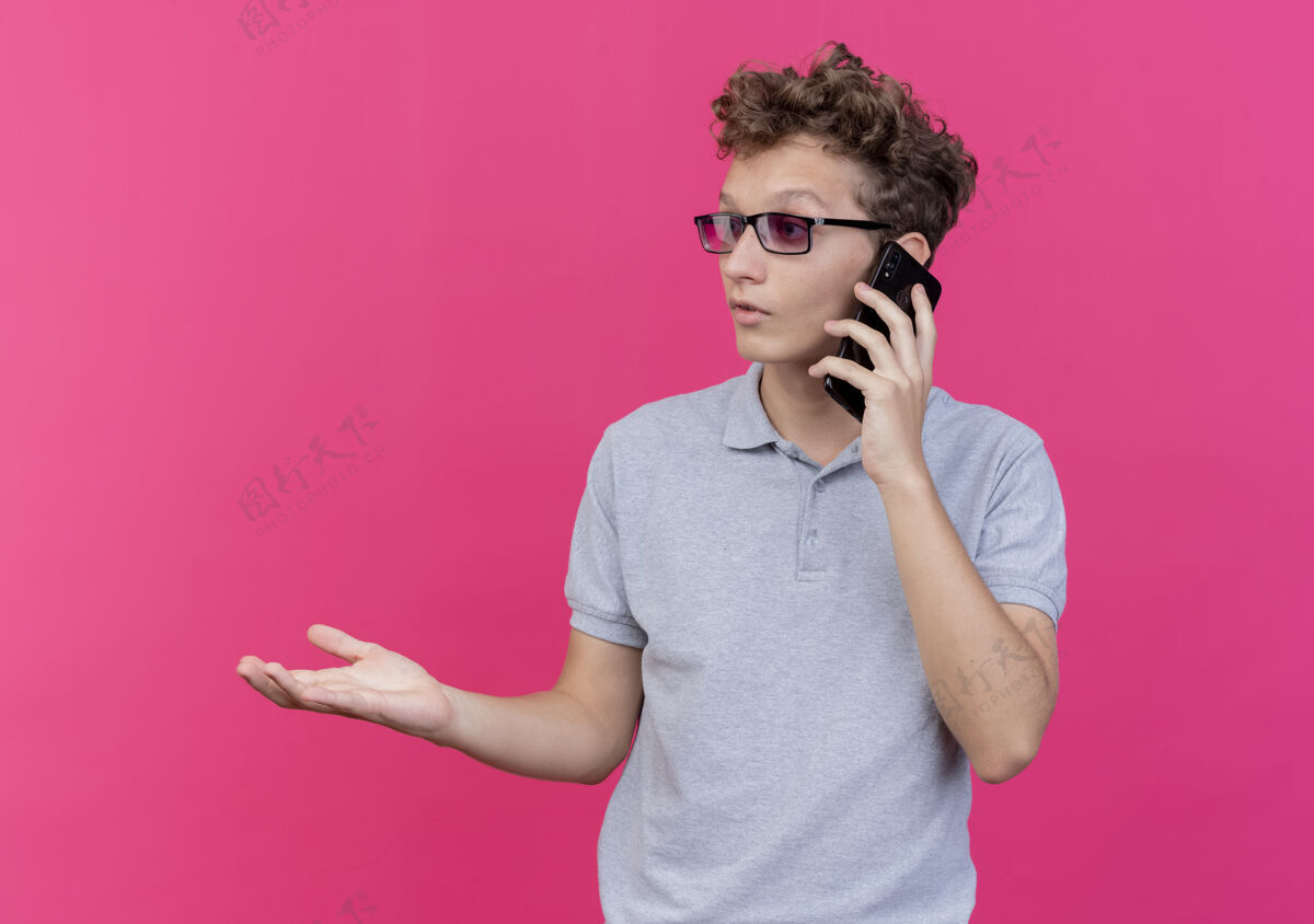 旁听一个戴着黑眼镜 穿着灰色马球衫的年轻人一边打电话一边伸出胳膊 一边问 一边为粉红色争吵衬衫辩会说话