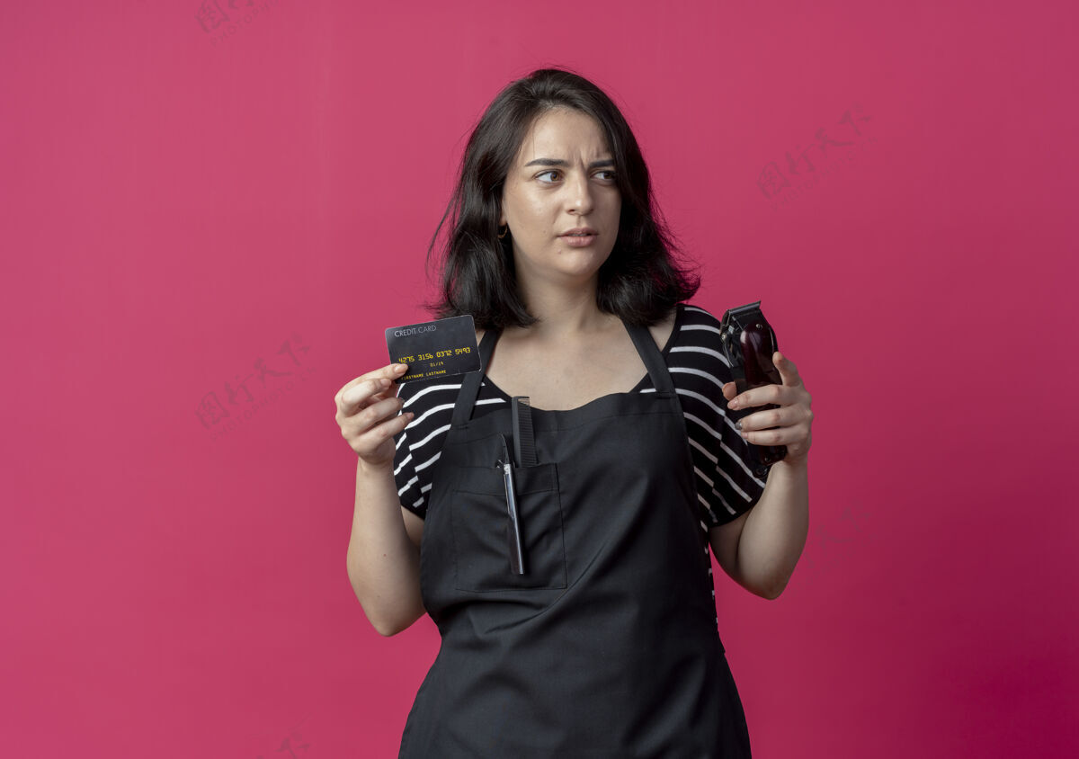 信用卡年轻漂亮的女理发师围着围裙拿着理发机和信用卡一边看一边迷惑不解的粉红色围裙卡片女性