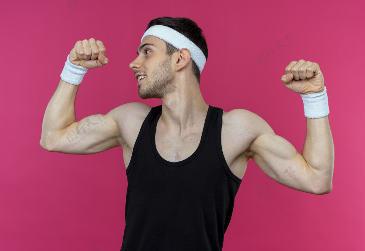 头带戴着头巾的年轻运动型男子举起拳头展示肱二头肌 胜利者概念胜过粉色二头肌男头