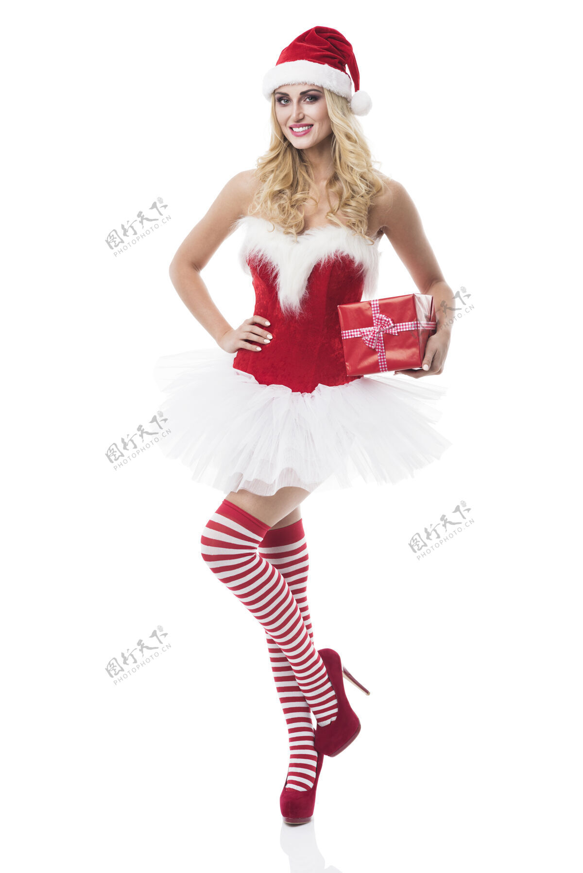 圣诞节穿着圣诞老人服装的性感女人在白墙上摆姿势新鲜圣诞礼物树双手放在臀部