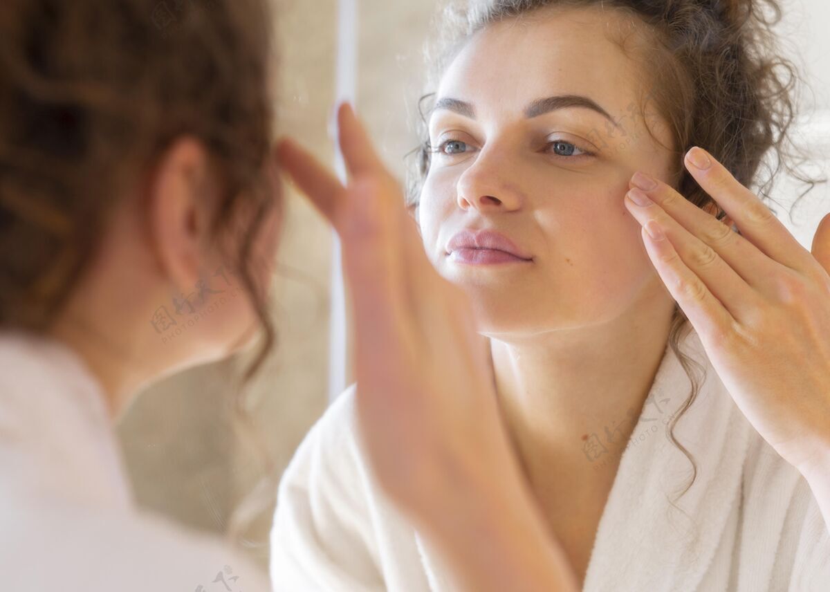 女人照镜子的时候在脸上涂面霜的女人美容面部护理女人