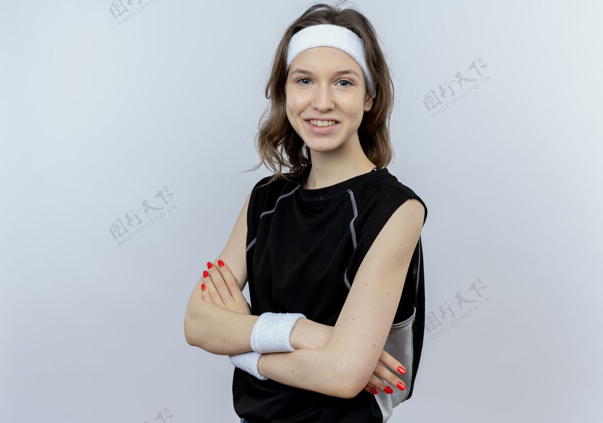 微笑身穿黑色运动服 头箍微笑 双手交叉站在白墙上的年轻健身女孩看年轻运动装