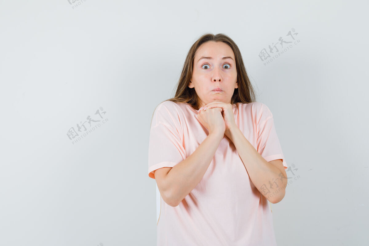 快乐年轻的女性穿着粉色t恤 双手紧握在下巴下 看上去很困惑 正前方的景色深色年轻成人
