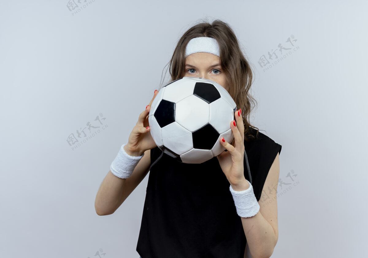 健身身穿黑色运动服的年轻健身女孩 头上戴着足球带 掩面站在白墙上脸球头带