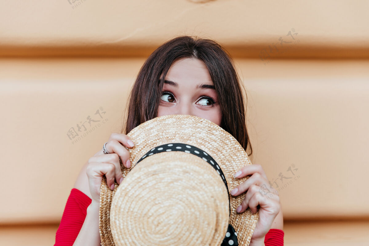 表情漂亮的高加索女人 手里拿着夏天的帽子 在户外鬼混黑发女人 脸上露出幸福的表情 在墙前摆姿势街道优雅漂亮
