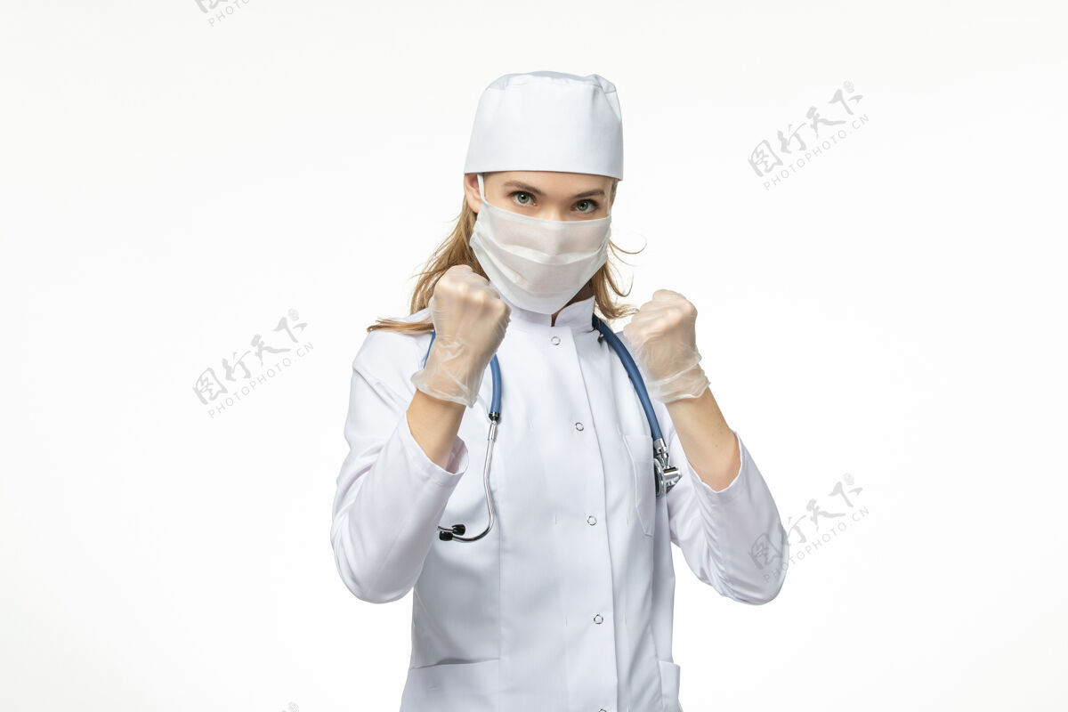 浅白色正面图女医生穿着医疗服 戴着口罩和手套 由于冠状病毒在战斗中摆出了轻白墙病大流行的冠状病毒的姿势冠状病毒防护女性大流行
