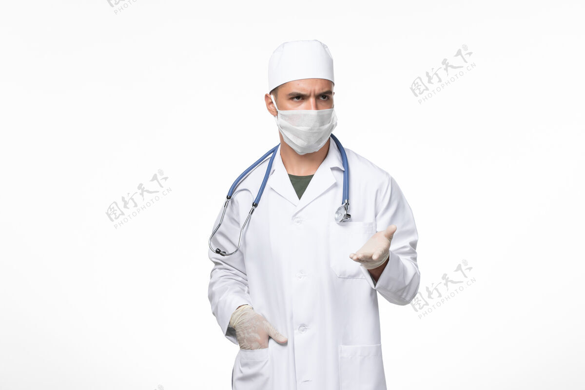 听诊器正面图：男医生穿着医疗服 戴着口罩抵御白色墙壁上的冠状病毒病大流行专业对抗查看