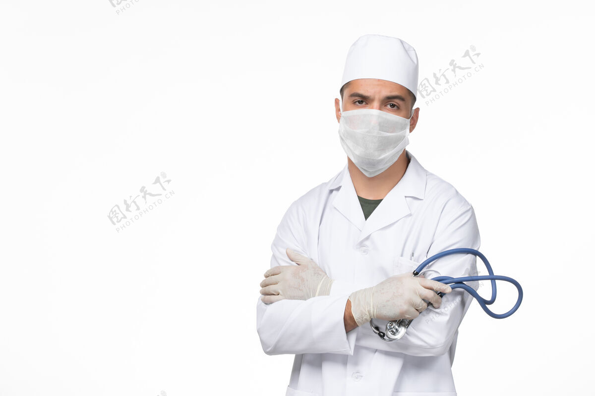 男性正面图：男医生身穿防毒服 戴口罩 手持听诊器 对白墙病毒冠状病毒-疾病大流行佩戴医疗持有