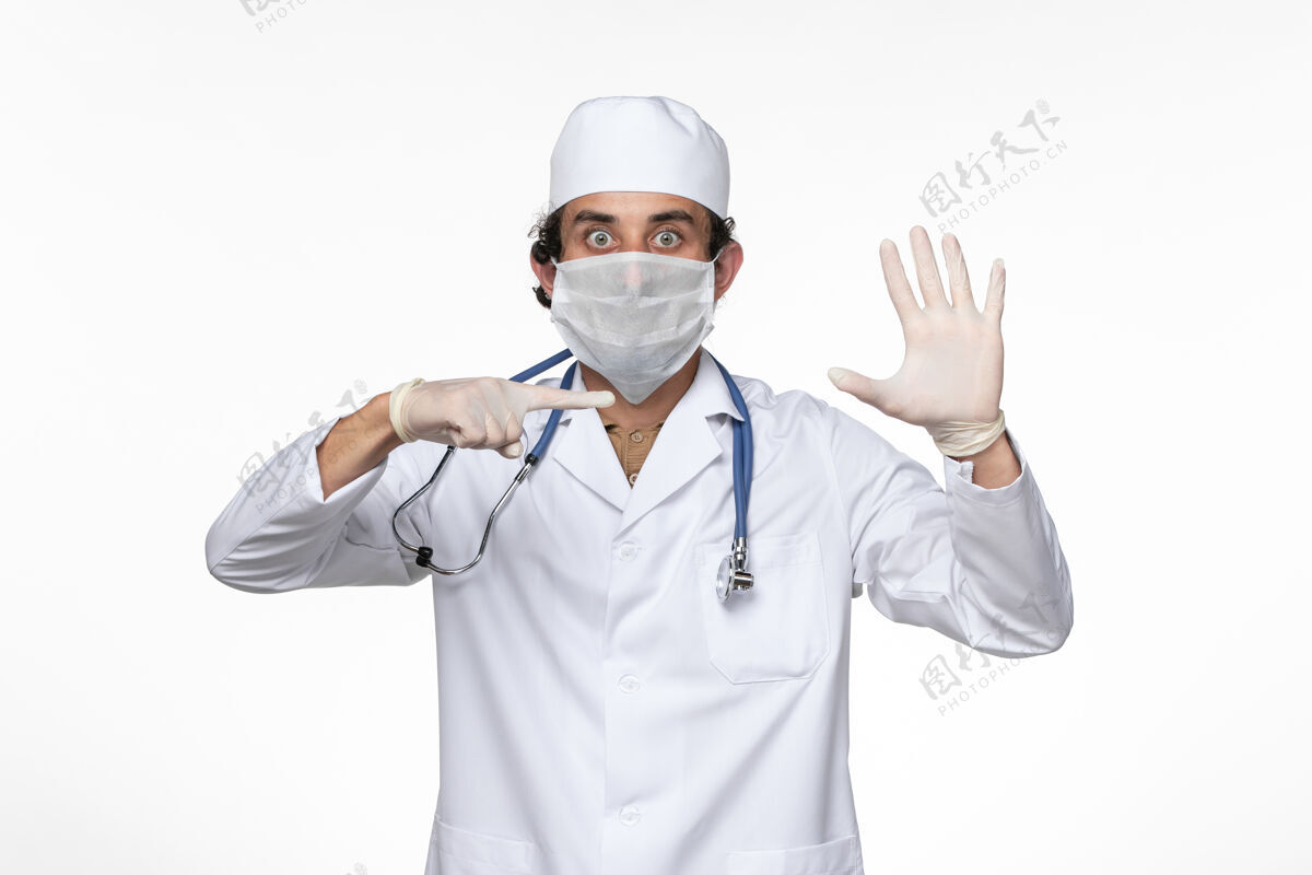 视图正面图身穿医疗服的男医生戴着无菌口罩 以防白色办公桌上的冠状病毒疾病冠状病毒大流行正面男人防护
