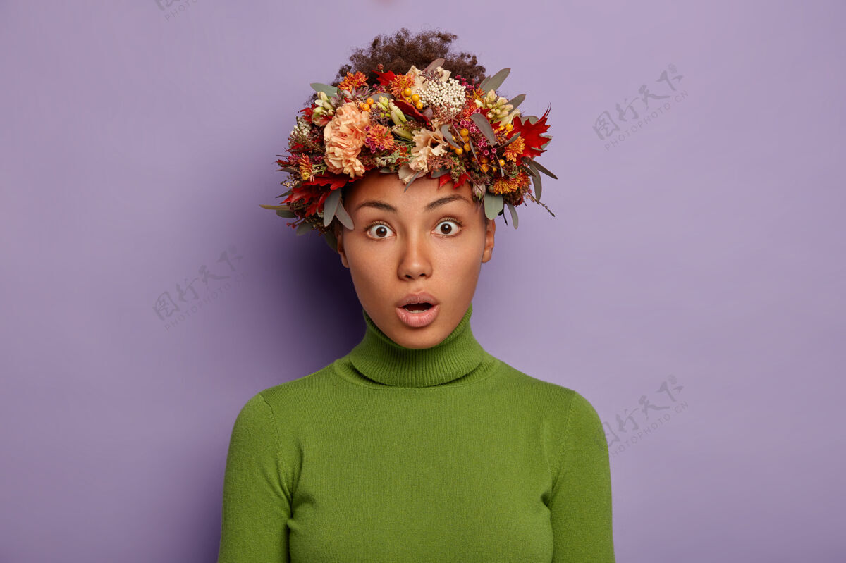 绿色迷人的卷发成年女子的肖像在镜头前震惊地看着 感到惊愕和惊讶 张大嘴巴 头戴秋天的花环 在紫色背景下的工作室里摆姿势哇紫色惊奇