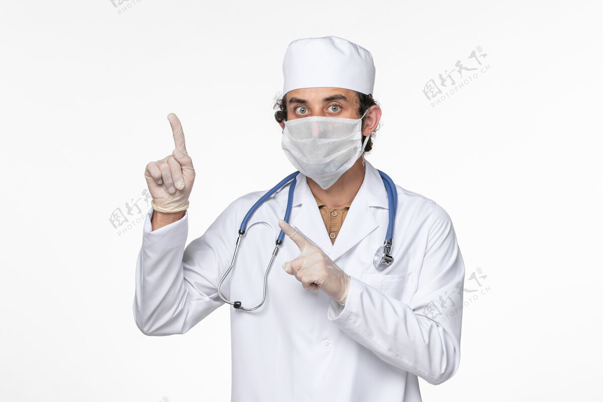 冠状病毒正面图身穿医疗服的男医生 戴着无菌口罩 以防感染冠状病毒-举起手指看白墙病毒大流行疾病医生病毒套装