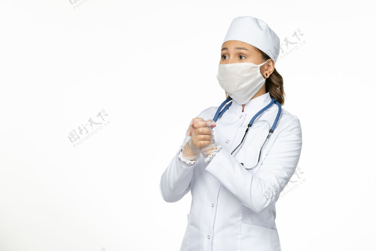 疾病正面图女医生身穿白色医疗服戴口罩因冠状病毒对淡白色墙壁大流行性疾病病毒隔离微笑光前面