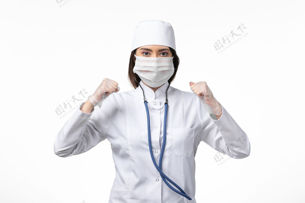 医生正面图女医生身穿白色无菌医疗服 带口罩 因白墙上冠状病毒病大流行冠状病毒面具医疗专业