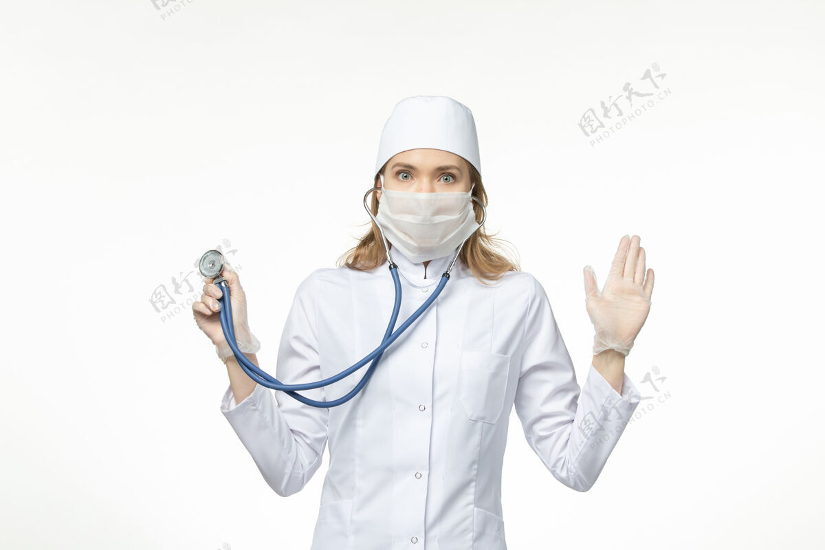 冠状病毒防护正面图女医生穿着医疗服戴口罩因冠状病毒手持听诊器对浅白壁病毒大流行冠状病毒-疾病到期病毒大流行