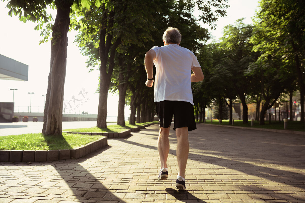 退休高级男子作为跑步者与袖标或健身追踪器在城市的街道老年人运动员健身
