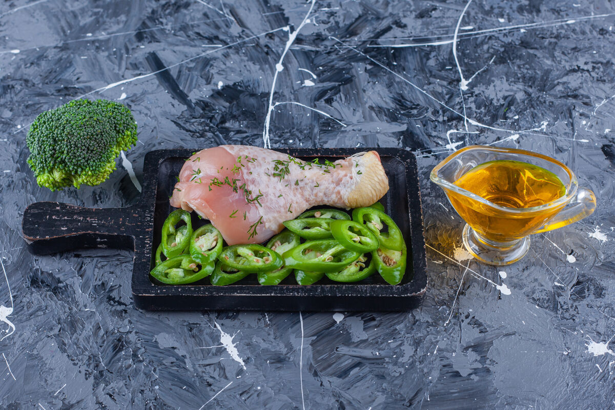 蛋白质把鸡腿和辣椒片放在一块木板上 旁边放上油和西兰花 放在蓝色的表面上有机开胃菜生的