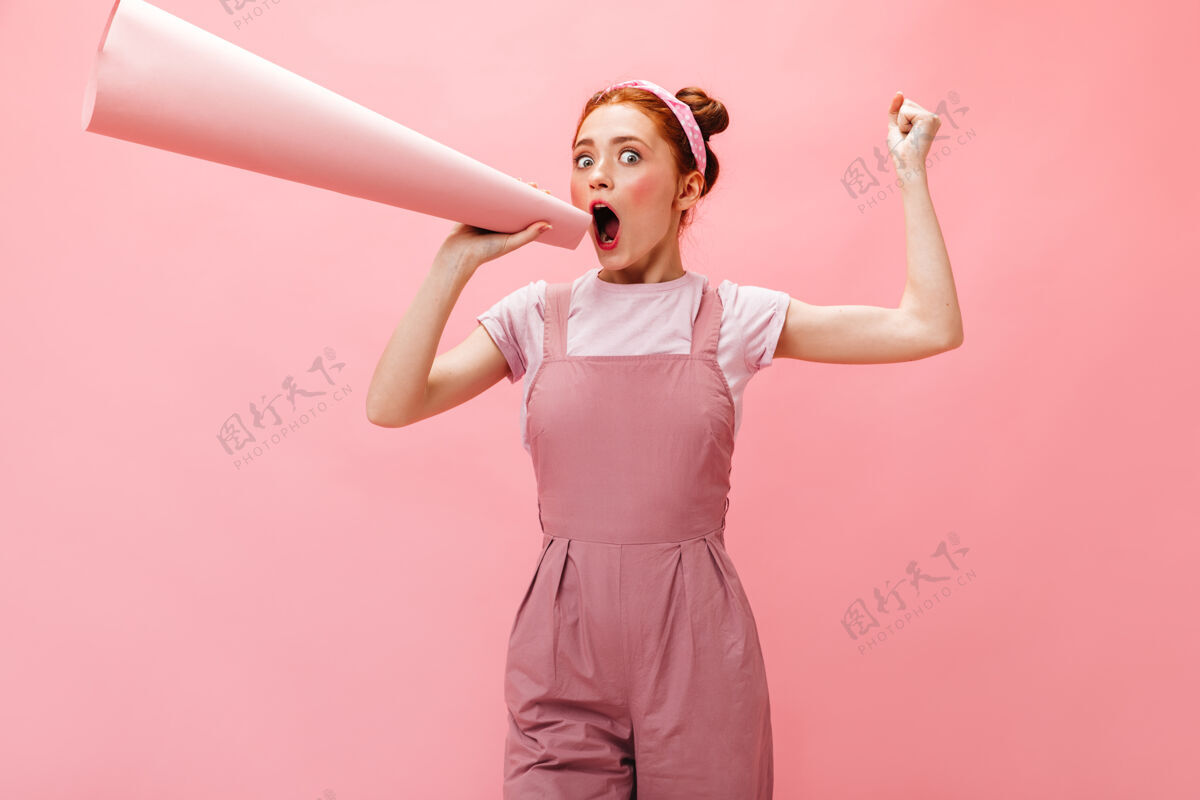 女性化身着粉色连衣裙和白色t恤的快乐年轻女士在粉色背景下对着话筒尖叫成人女人美女