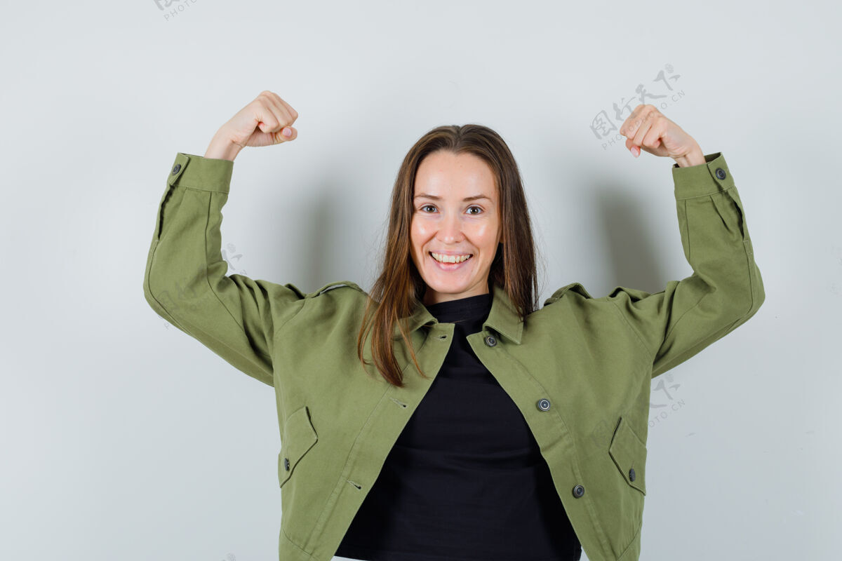 女人身着绿色夹克展示手臂肌肉的年轻女子 看上去很有力量 正面视图肌肉休闲年轻