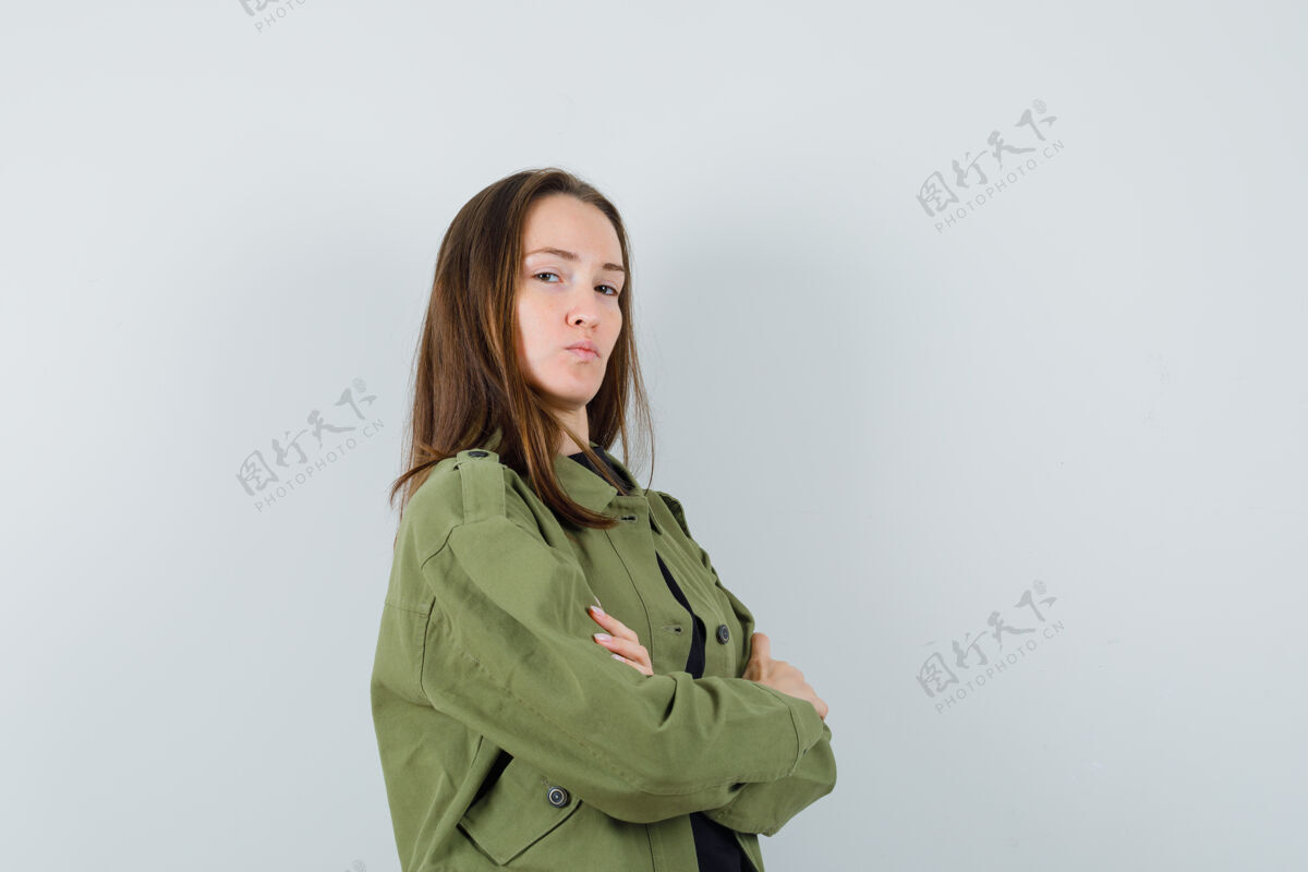 积极年轻女子交叉着双臂站在一旁 穿着绿色夹克 黑色衬衫 看起来很自夸 正面照时尚休闲女人
